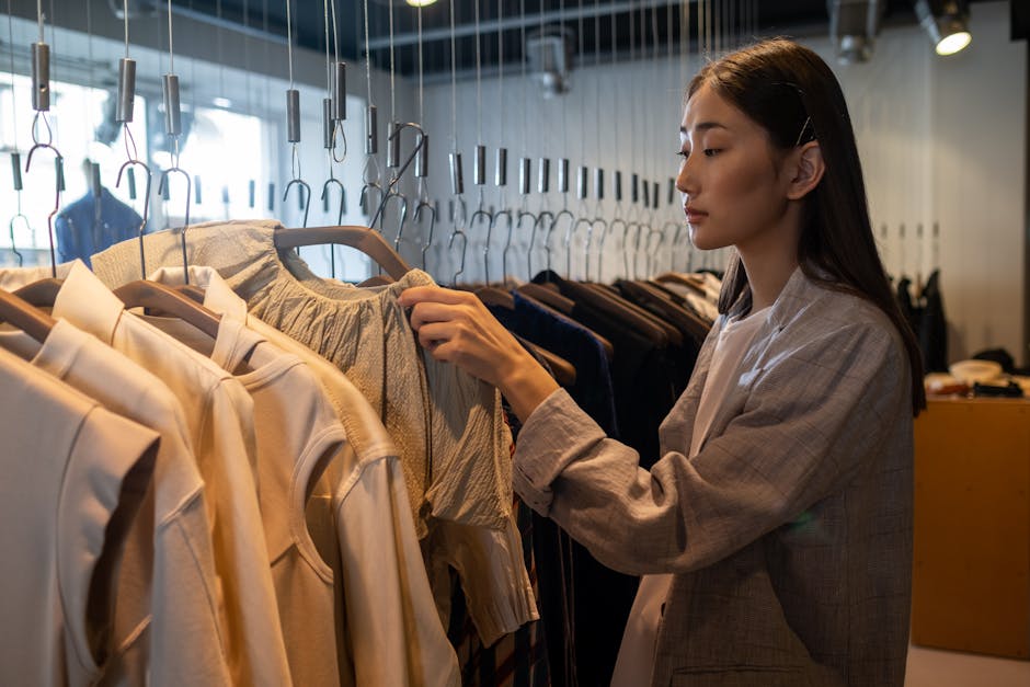 An Asian woman browsing clothing in a boutique shop, examining fashion items on hangers.