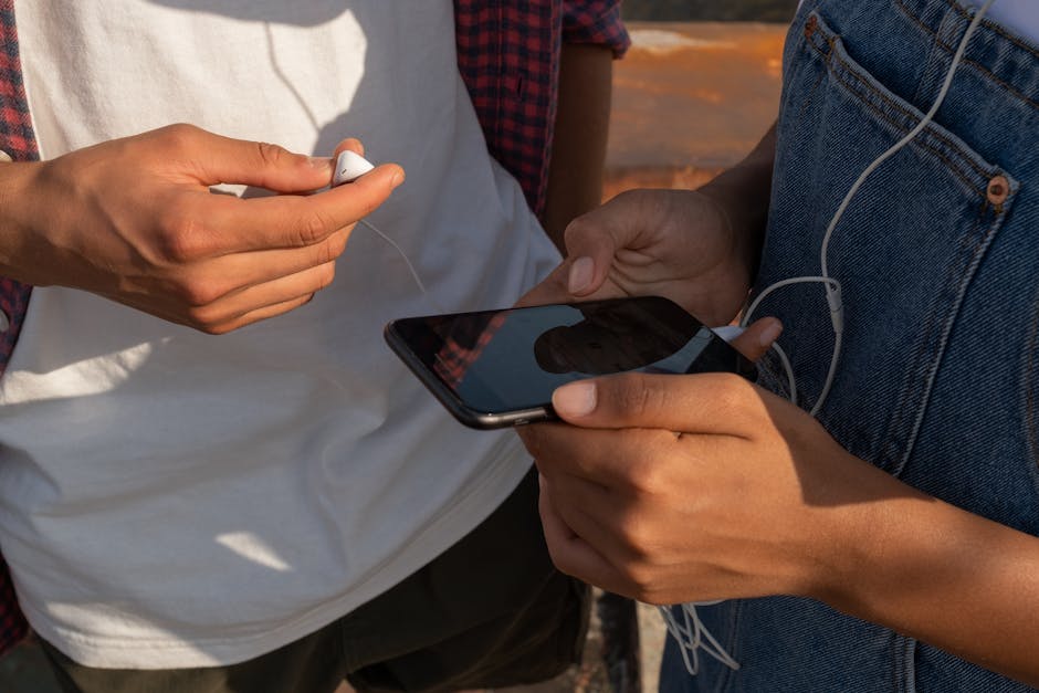 Close-up of teenagers sharing music on a smartphone outdoors with earphones.