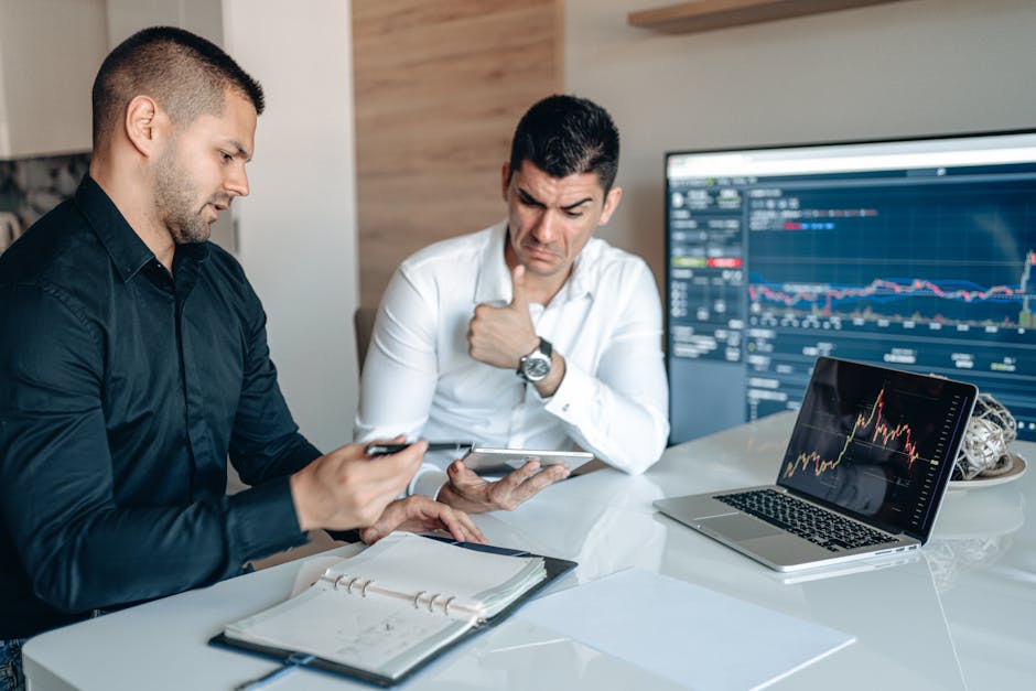 Two professionals discuss data analysis on digital devices in an office setting, focusing on graphs and charts.